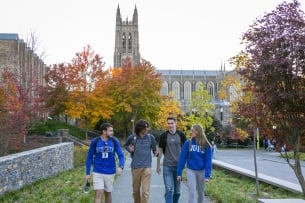 Four Duke students walk on campus in front of the chapel tower.