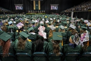 Students face away from the camera wearing green graduation robes during the Wright State University spring 2024 commencement ceremony.