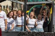 A group of women wearing matching white shirts smile on a parade float