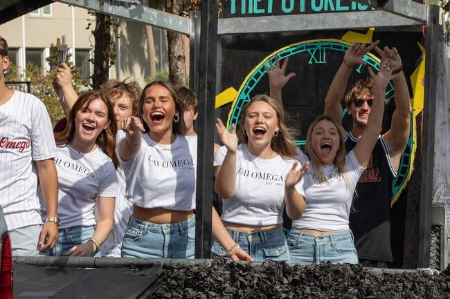 A group of women wearing matching white shirts smile on a parade float