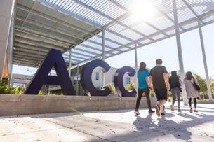 Students walk in front of a sign that reads "ACC" in large navy blue letters. 