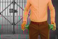 A student in business attire turns out their empty pockets in front of a closed college gate.