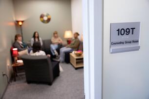 Sign indicating "Counseling Group Room" outside of a room where a group is meeting on a college campus.