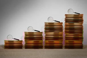 Stacks of files getting taller each with a magnifying glass sitting on them.
