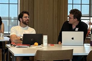 Two men work at laptops in conversation