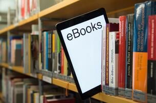 A tablet with the word "ebooks" peeks out from a library shelf lined with physical books.