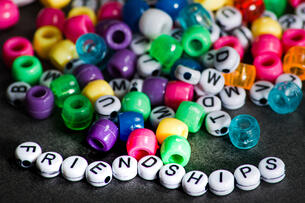 The word "friendships" is spelled out in beads, with other scattered beads of different colors, some with letters, some without, strewn in the background.
