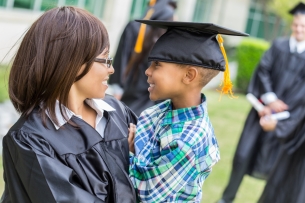A student in her graduation robe holds her child, who is wearing her mortarboard.
