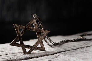 A Star of David pendant sits on an old wooden table against a black background.