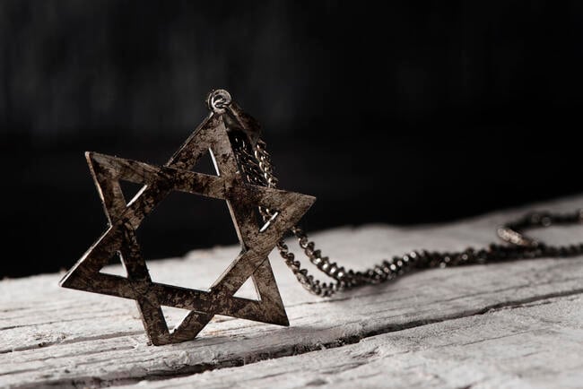 A Star of David pendant sits on an old wooden table against a black background.