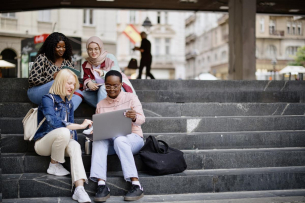 Students sit on the steps near the college and look at the laptop and digital tablet and talk
