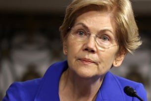 Elizabeth Warren, a light-skinned woman with short blond hair, wearing glasses and a deep blue-purple jacket.