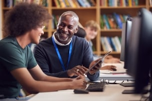 A male staff member helps a young male student on a library computer
