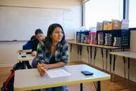 A student sits at a desk holding a pencil. 