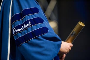 The president of a university holding the next student's diploma.