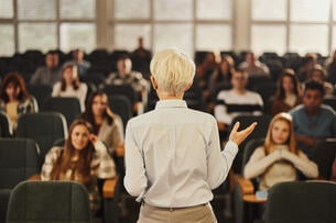 A photo from the back of a female professor teaching a lecture hall full of students.