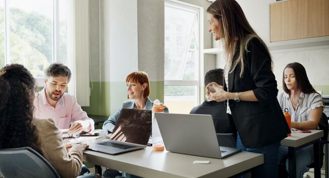 A smiling university instructor assists a small group of students with a project in the classroom.