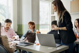 A smiling university instructor assists a small group of students with a project in the classroom.