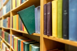 A photo of a library book shelf, with a single green book sticking out amid the other volumes.