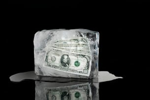 Money frozen in a block of ice against a black background.