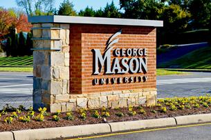A photo of a brick entrance sign for George Mason University, along a roadway.