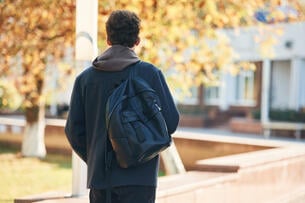 Young student is outside the university, in black clothes