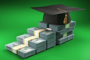 Stacks of U.S. dollars of different heights are lined up to create the impression of an ascending staircase; a graduation cap with tassel sits on the top level.