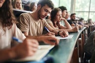 A university student and his classmates write during a class in a lecture hall.