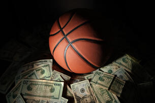 A basketball and a pile of cash against a dark background.