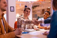 Young applicants shaking hands with a manager during a job interview in a modern office setting, exchanging smiles while discussing career opportunities and building professional connections