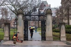 A person holding a yellow umbrella walks under a gate at Brown University