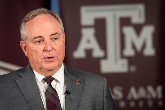 Mark Welsh in jacket and tie in front of Texas A&M sign