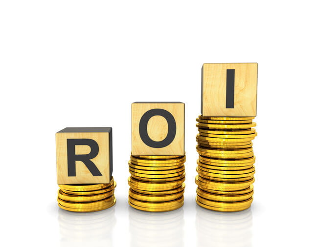 Three wooden alphabet blocks that together spell "ROI" sit atop three stacks of gold coins.