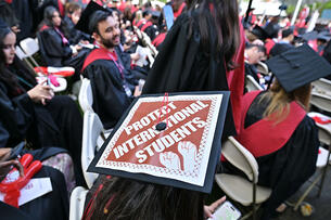 A Harvard University graduate with a message in support of international students on her mortarboard sits with fellow students at the start of commencement exercises.