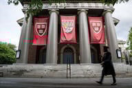 A photo of the Harvard campus with a graduate walking by.