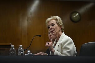 Linda McMahon, an older white woman wearing a white blazer, sits at a table in a hearing room in the Capitol