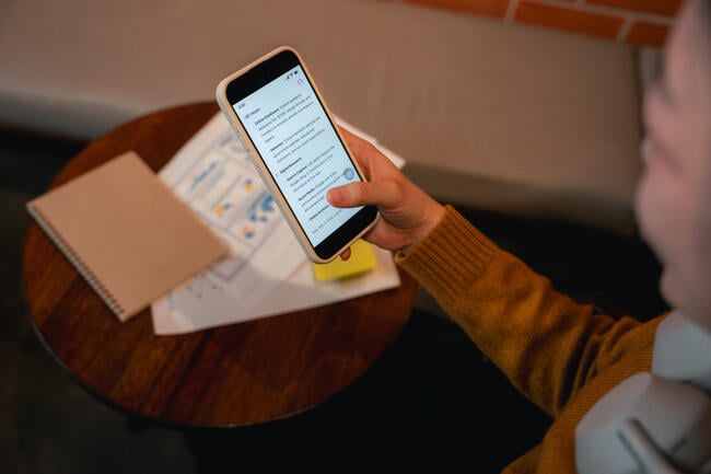 A close-up of a college student using an AI app on her smartphone in a semi-darkened room.