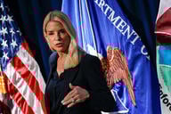 Attorney General Pam Bondi stands in front of flags and holds her hand up
