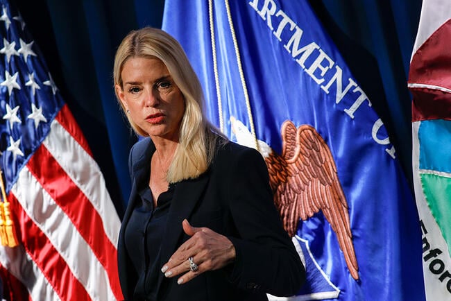 Attorney General Pam Bondi stands in front of flags and holds her hand up