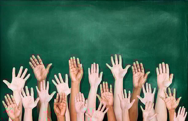 Multiethnic group of raised hands in front of a green chalkboard.