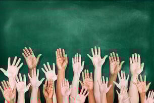 Multiethnic group of raised hands in front of a green chalkboard.