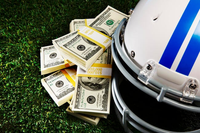 Stacks of $100 bills sit next to a football helmet atop a field.