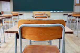 A photo of an empty classroom, taken from the back of the room, with a chair and desk combination most prominent in the center of the frame.