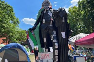 A statute of George Washington is covered in a stickers, a Palestinian flag and keffiyeh.