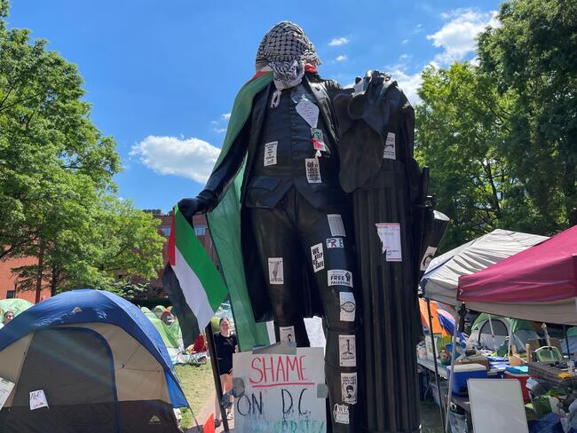 A statute of George Washington is covered in a stickers, a Palestinian flag and keffiyeh.