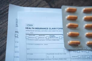 two health insurance claim forms and a packet of orange pills