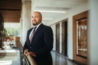 Portrait of Julian Vasquez Heilig, a man with light brown skin, a bald head and a beard, wearing a suit and tie.