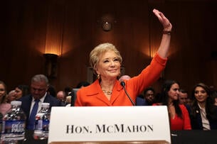 Linda McMahon, wearing an orange suit, sits behind her name card at her confirmation hearing.