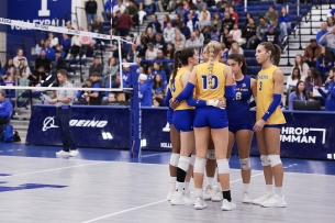 Several athletes huddle on a volleyball court.