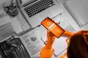 A student using AI on a cellphone at a desk covered in study materials.